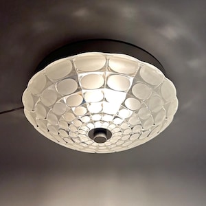 Pode incluir: Uma luminária de teto branca com um abajur redondo de vidro fosco. O abajur tem um padrão de pequenos círculos em relevo.