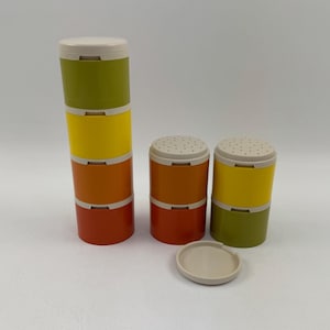 May include: Set of four vintage spice jars with a retro design. The jars are stacked in a tower with a separate lid. The jars are orange, yellow, and green.