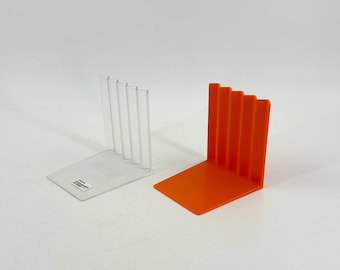 May include: Two bookends, one clear plastic and one orange plastic. Both bookends have a vertical design with multiple ridges.
