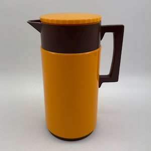May include: A retro-style thermos flask in orange and brown. The cylindrical flask has a bright orange body, a dark brown top section, handle, and lid. The lid is a lighter shade of orange. Designed for keeping drinks hot or cold.