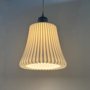 May include: A white pendant light fixture featuring a bell-shaped shade with vertical ribbed textures. The lamp is suspended by a thin white cord and emits a soft, warm glow from the bottom opening, highlighting the fluted exterior design.