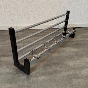 Op de afbeelding: Een zwart en zilverkleurig metalen kapstok met een minimalistisch design. De kapstok heeft een rechthoekig zwart frame met horizontale zilveren stangen om jassen op te hangen en een rij zilveren haken. Het ontwerp is eenvoudig en modern.