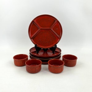 Op de afbeelding: Een set rode keramische serveerschalen met een decoratief ontwerp. De set bevat een grote, verdeelde schotel en vier kleine kommen.