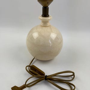 Peut inclure: Une lampe de table sph&eacute;rique cr&egrave;me avec un motif marbr&eacute;. La lampe a une base marron et une douille marron. Un cordon d'alimentation marron avec un interrupteur et une prise s'&eacute;tend de la lampe.