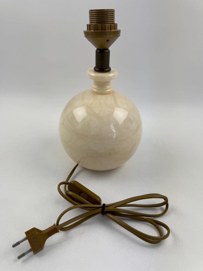Peut inclure: Une lampe de table sph&eacute;rique cr&egrave;me avec un motif marbr&eacute;. La lampe a une base marron et une douille marron. Un cordon d'alimentation marron avec un interrupteur et une prise s'&eacute;tend de la lampe.
