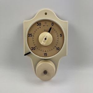 Può includere: Un timer da cucina vintage color crema con un quadrante circolare e un campanello. Il quadrante presenta numeri e segni neri, con una manopola centrale e una lancetta nera che indica l'ora. Il timer è progettato per misurare fino a 30 minuti.