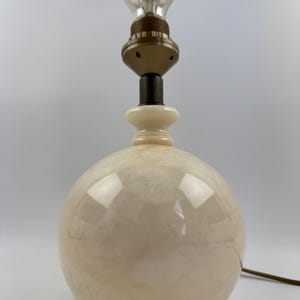 Peut inclure: Une lampe de table sph&eacute;rique cr&egrave;me avec une ampoule de style vintage. La lampe a une base ronde et une douille de couleur laiton. L'ampoule est transparente avec un filament visible. Un cordon &eacute;lectrique marron s'&eacute;tend de la base.