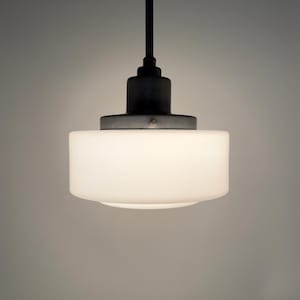 Puede incluir: Una moderna lámpara colgante con una pantalla cilíndrica de vidrio blanco y un vástago y dosel de metal oscuro. La luz cuelga del techo, proyectando un brillo suave. El diseño es minimalista y adecuado para varios estilos de interior.