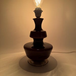May include: A dark brown glass table lamp with a layered design and a silver base. The lamp is switched on and the light bulb is glowing.