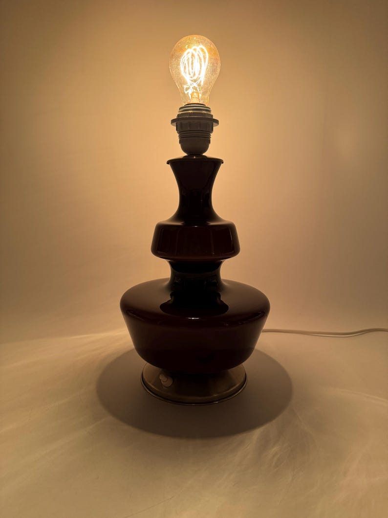 May include: A dark brown glass table lamp with a layered design and a silver base. The lamp is switched on and the light bulb is glowing.