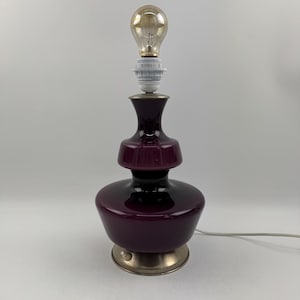 May include: A purple glass table lamp with a silver base and a light bulb. The lamp has a layered design with a wide base and a narrow neck.