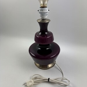 May include: A purple glass table lamp with a brass base and a white cord. The lamp has a round, bulbous shape and a simple design.