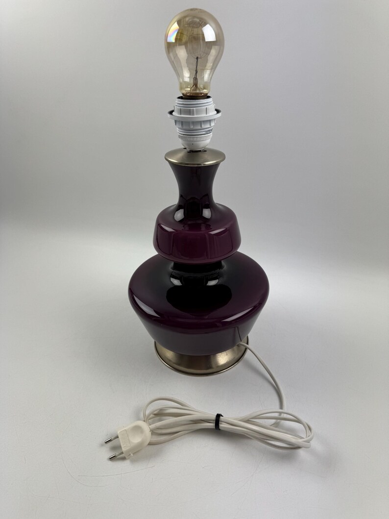 May include: A purple glass table lamp with a brass base and a white cord. The lamp has a round, bulbous shape and a simple design.