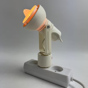 May include: A white, adjustable desk lamp with a round, orange-lit shade. The lamp is connected to a white power strip with two sockets and a white cord. The lamp's design is minimalist and modern.