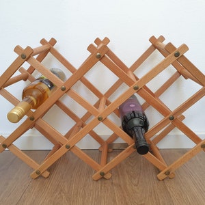 May include: A wooden wine rack with a diamond pattern holds two bottles of wine. One bottle is white wine and the other is red wine.