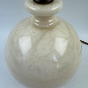 Peut inclure: Gros plan sur un pied de lampe sph&eacute;rique cr&egrave;me avec un motif marbr&eacute;. La base a un dessus arrondi et un col brun fonc&eacute;. Un cordon &eacute;lectrique marron s'&eacute;tend de la base.