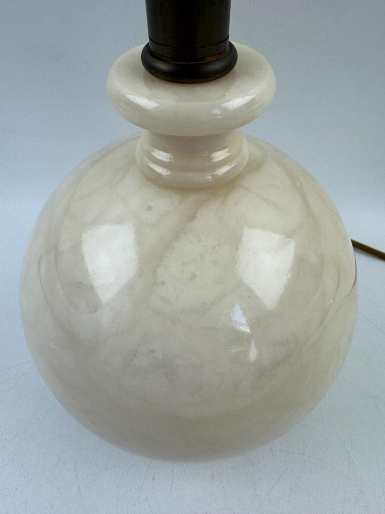 Peut inclure: Gros plan sur un pied de lampe sph&eacute;rique cr&egrave;me avec un motif marbr&eacute;. La base a un dessus arrondi et un col brun fonc&eacute;. Un cordon &eacute;lectrique marron s'&eacute;tend de la base.