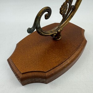 May include: A decorative wall-mounted display piece. It features a dark wood base with a curved, ornate metal accent in shades of gold and verdigris. The metalwork includes floral and scroll designs.