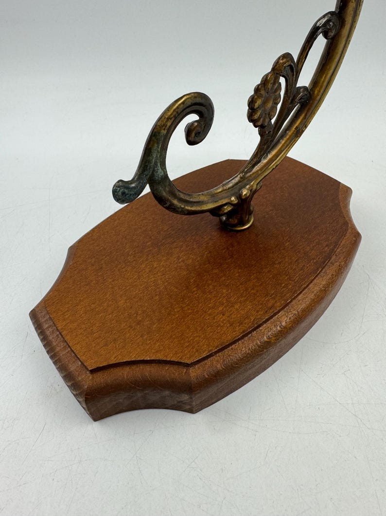 May include: A decorative wall-mounted display piece. It features a dark wood base with a curved, ornate metal accent in shades of gold and verdigris. The metalwork includes floral and scroll designs.