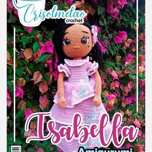 Puede incluir: Una muñeca amigurumi de crochet llamada Isabella, con piel morena, cabello negro y un vestido rosa con detalles florales. La muñeca está posada sobre un fondo de flores rosas.