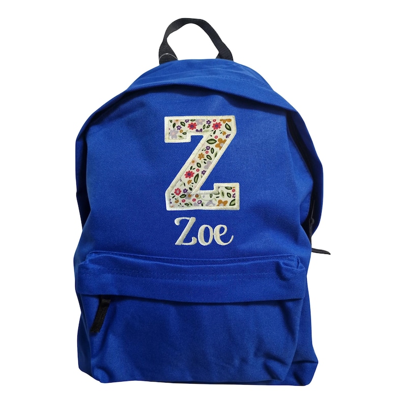 May include: A royal blue backpack featuring a large letter Z patch with a colorful floral pattern. Below the letter, the name Zoe is embroidered in white script. The backpack includes a top handle and a front zippered pocket for storage.