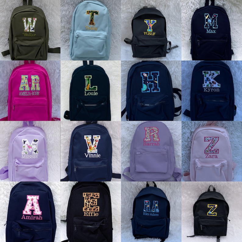 May include: A collection of sixteen backpacks in various solid colors, each featuring a large embroidered initial letter with a patterned fill and a personalized name stitched underneath. The backpacks include front zippered pockets and shoulder straps.