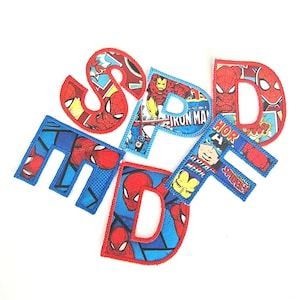 May include: Embroidered fabric letters spelling out SPIDER-MAN. The letters are in red and blue, featuring Spider-Man and other Marvel comic book characters. The letters are on a white background.