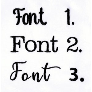 May include: Three distinct black embroidered text samples on a white fabric background. The first line reads Font 1, the second line reads Font 2, and the third line reads Font 3. Each line displays a different typeface style in black thread.