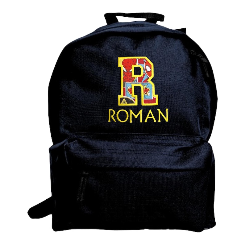 May include: A navy blue backpack featuring a large embroidered letter R with a red and blue superhero comic book pattern inside the letter. Below the letter R, the name ROMAN is embroidered in yellow capital letters on the front pocket.