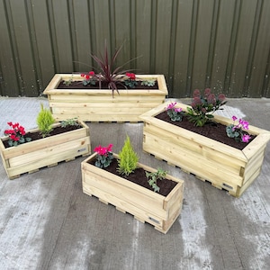 May include: Four wooden planter boxes in various sizes, filled with plants and flowers. The boxes are made of natural wood and have a rustic look.