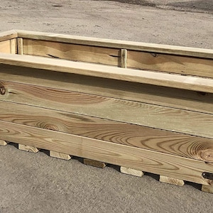 May include: A rectangular wooden planter box made from natural wood planks. The planter has a raised lip around the top and a simple, rustic design.
