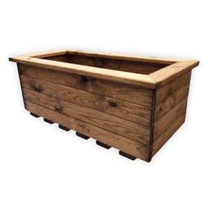 May include: A rectangular wooden planter box with a natural wood finish. The box is constructed from horizontal planks and features a raised rim around the top. The base has several supporting slats. Ideal for outdoor or indoor plants.