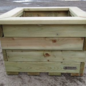 May include: A square wooden planter box with a natural wood finish. The planter is made of multiple layers of wood and has a small metal tag on the bottom right side that says "Sentry Wood".