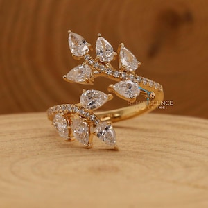 Op de afbeelding: Een gouden ring met een delicaat ontwerp met een tak met peervormige diamanten. De ring is bezet met kleine diamanten langs de band en heeft een uniek, open ontwerp.