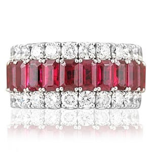 Pode incluir: Um anel de prata com três fileiras de pedras preciosas. A fileira central apresenta rubis vermelhos escuros retangulares, enquanto as fileiras superior e inferior são adornadas com diamantes redondos e transparentes. O anel está sobre um fundo branco.