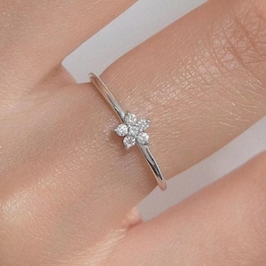 Op de afbeelding: Een delicate zilveren ring met een bloemmotief. De bloem is samengesteld uit kleine, sprankelende edelstenen. De ring heeft een dunne band en een minimalistische uitstraling.