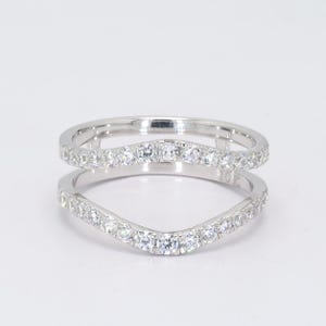May include: A 10K white gold ring guard featuring two curved bands connected by vertical bars. Both bands are pavé-set with numerous small, clear, round-cut stones that extend across the front. The metal is polished and reflective.