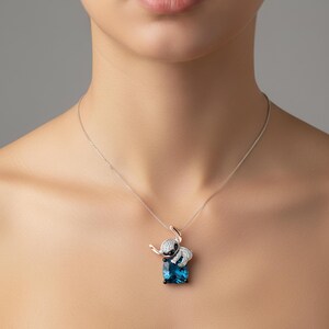 Pu&ograve; includere: Una collana d'argento con un ciondolo a forma di elefante. L'elefante ha un design bianco e nero ed &egrave; appoggiato su una gemma blu rettangolare. La collana &egrave; indossata da una persona.