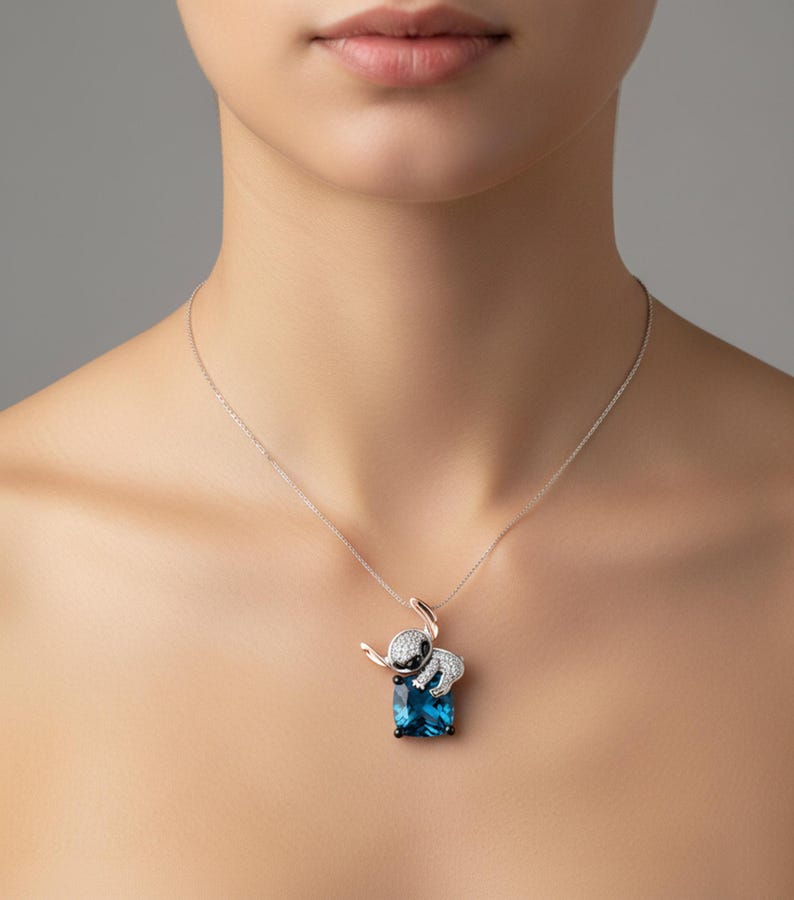 Pu&ograve; includere: Una collana d'argento con un ciondolo a forma di elefante. L'elefante ha un design bianco e nero ed &egrave; appoggiato su una gemma blu rettangolare. La collana &egrave; indossata da una persona.