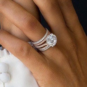 May include: A close-up of a hand wearing a rose gold engagement ring with a large, round, center diamond. The ring is surrounded by a band of smaller diamonds and two additional bands of smaller diamonds.
