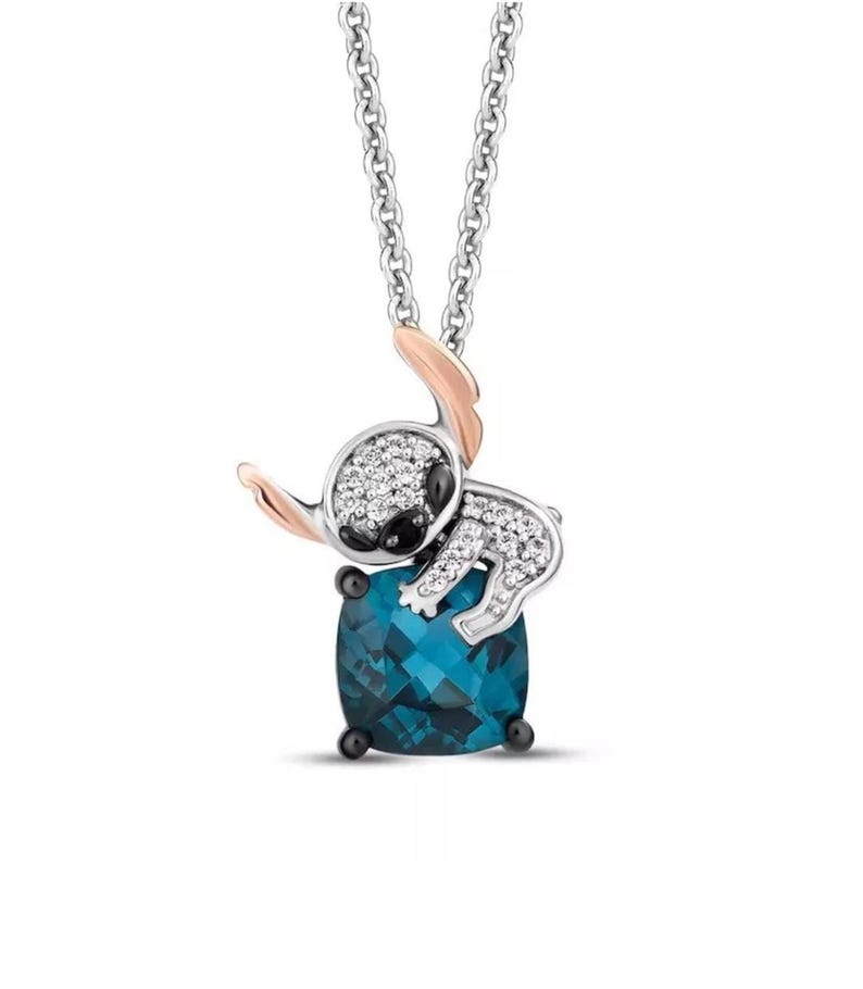 Pu&ograve; includere: Collana d'argento con un ciondolo raffigurante un personaggio dei cartoni animati. Il ciondolo ha una base di pietra preziosa blu, un personaggio ornato di cristalli trasparenti, dettagli in oro rosa e una catena d'argento.