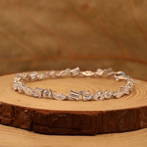 Puede incluir: Una pulsera de plata con una fila de piedras preciosas transparentes y facetadas de diferentes formas, incluyendo redondas, ovaladas y baguette.