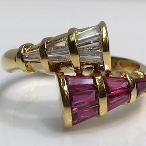 May include: A gold ring featuring two baguette-cut gemstone clusters. One cluster has clear stones, the other has pink stones. The ring has a twisted design with gold bands around the gemstone clusters.