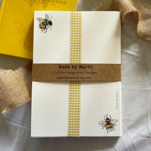 May include: Cream A5 writing sheets with a yellow gingham ribbon and bee illustrations. The band reads "Made by Marti" with the Etsy shop URL. A yellow book and honey dipper are in the background. The writing sheets are approximately 14.8 x 21 cm.