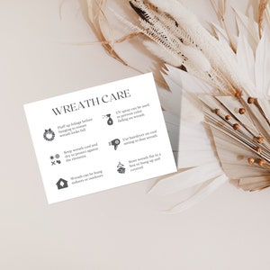 May include: A white card with the text "WREATH CARE" and care instructions for wreaths. The instructions include fluffing foliage, keeping the wreath cool and dry, and using UV spray. The card is surrounded by dried flowers.