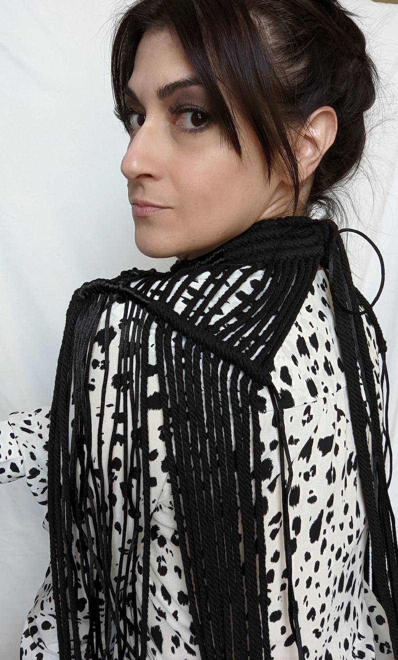 May include: A black macrame fringe scarf with a geometric pattern. The scarf is worn over a white and black animal print blouse.
