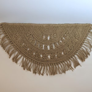 May include: A large, brown, macrame wall hanging with a fringe border. The hanging is in the shape of a half circle and features a geometric pattern.