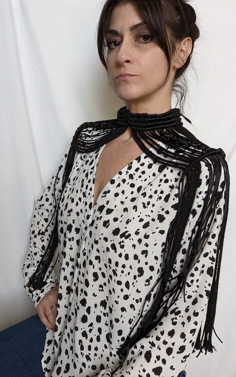 May include: A black and white animal print blouse with a black macrame choker and matching shoulder straps. The straps have long fringe details.