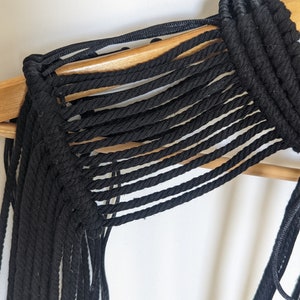 May include: Black macrame top with a fringe detail. The top is made of thick black cord and has a loose, flowing fit.