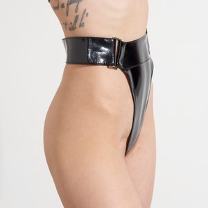 Puede incluir: Ropa interior de talle alto de cuero patentado negro con pierna de corte alto y cierre de hebilla.